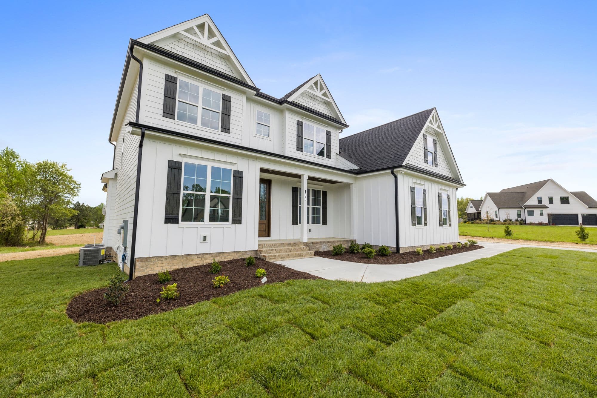 White modern farmhouse with black-framed windows, black shutters, and a covered front porch under a clear blue sky