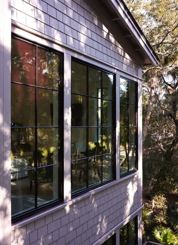 Black-framed grid windows on a shingle-sided coastal home, framed by palms and live oaks