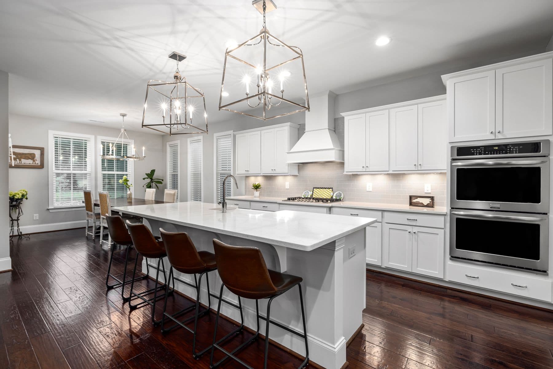 A bright white transitional kitchen with a large marble island and lantern pendants