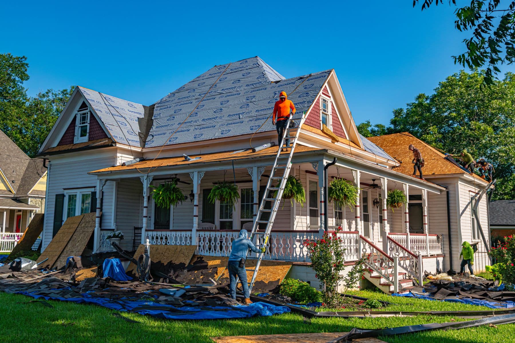 A crew working on the roof of a white porch-front home during a renovation